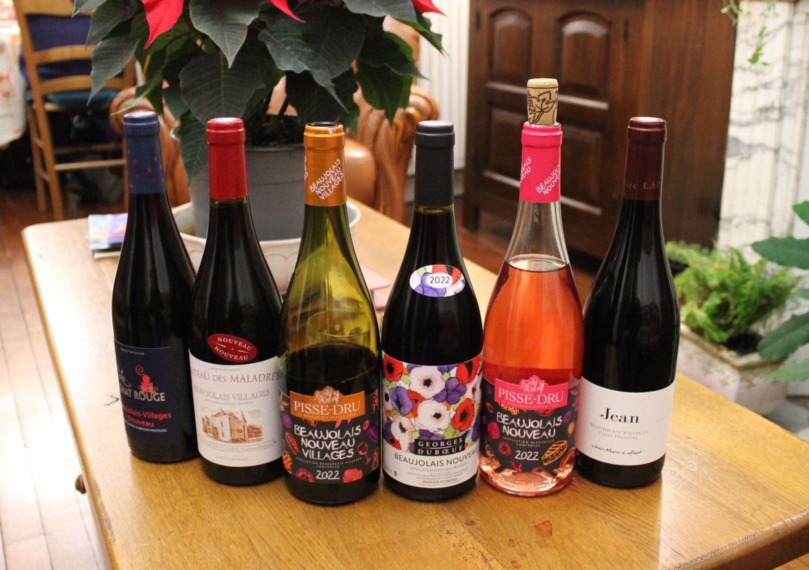 Six bouteilles de Beaujolais Nouveau et Beaujolais-Villages Nouveau alignées sur une table, dont un rosé