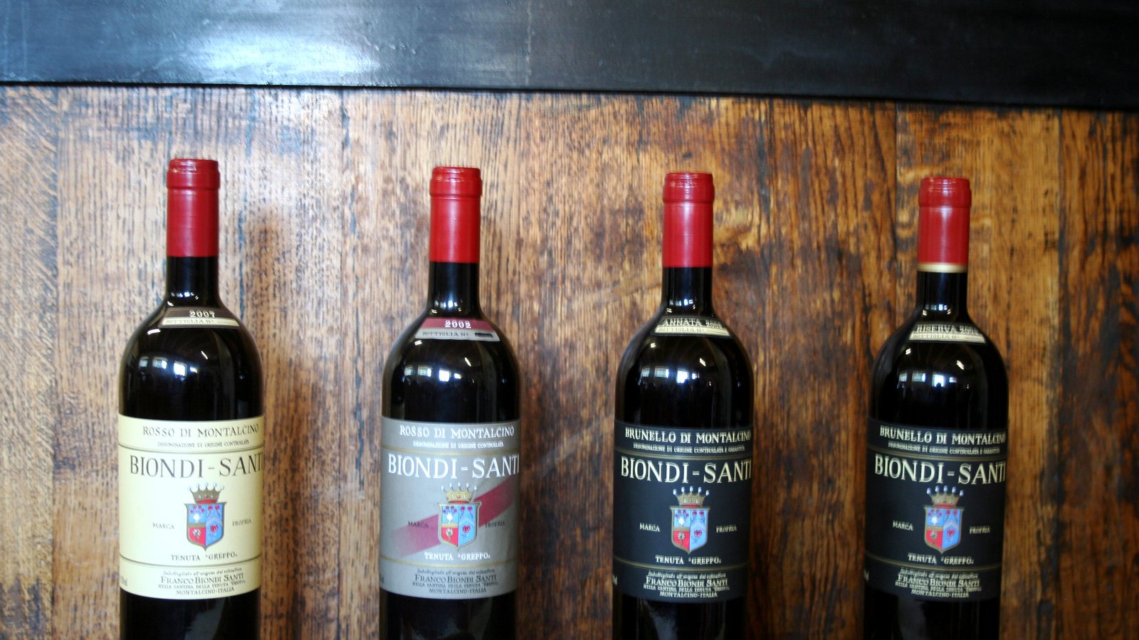 Quatre bouteilles Biondi-Santi, Rosso et Brunello di Montalcino, alignées devant un fût