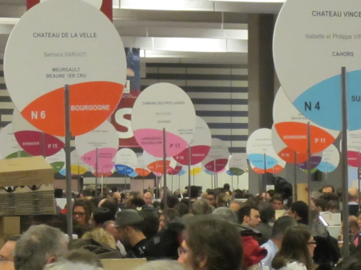 Allée fréquentée et panneaux de domaines colorés par région viticole à Paris en 2013.